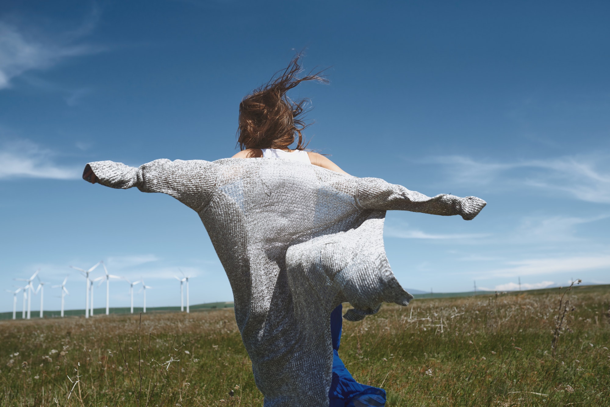 Woman with long tousled hair next to the wind turbine with the wind blowing