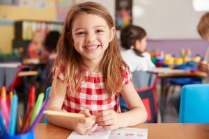 Portrait Of Smiling Female Elementary School Pupil Working At Desk