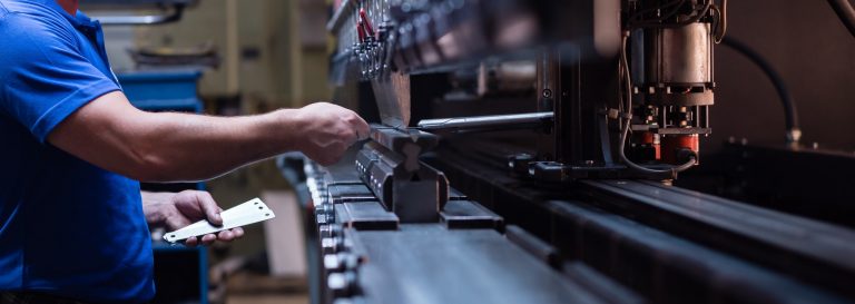 worker holding metal plate against manufacturing machinery