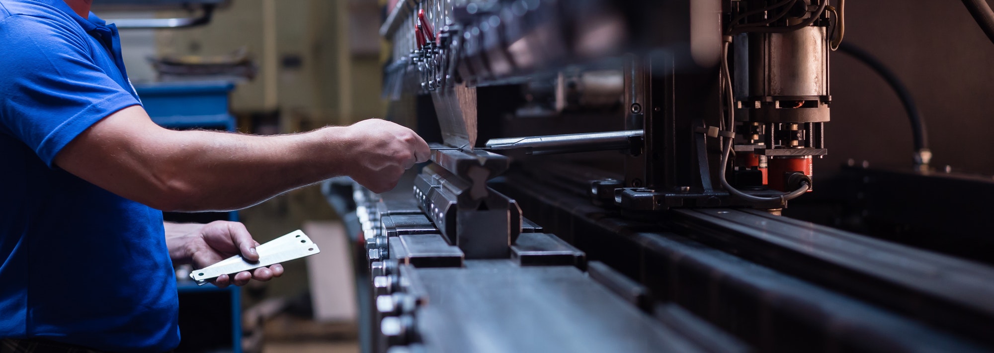 worker holding metal plate against manufacturing machinery